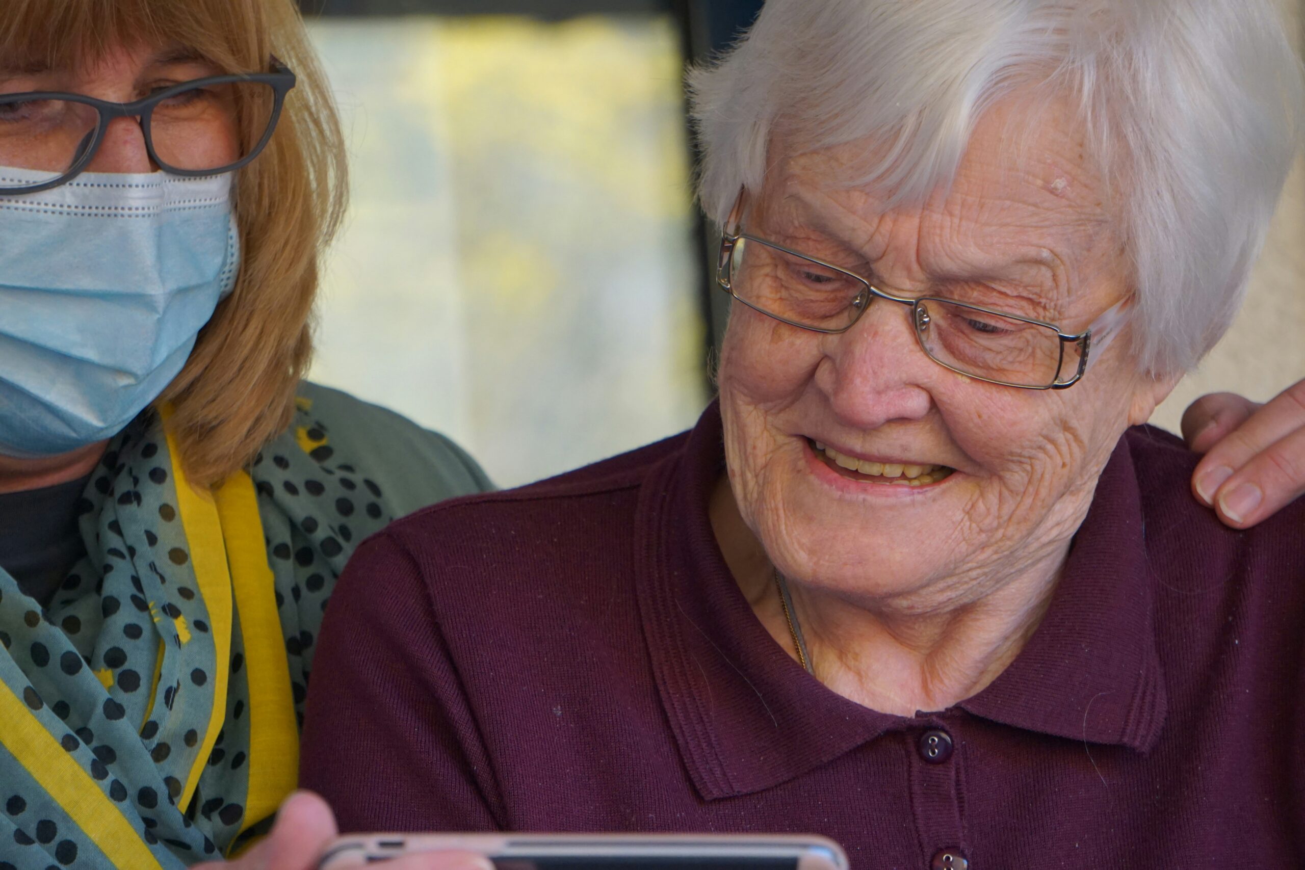 Elderly lady looking at tablet while supported by a mask-wearing nurse